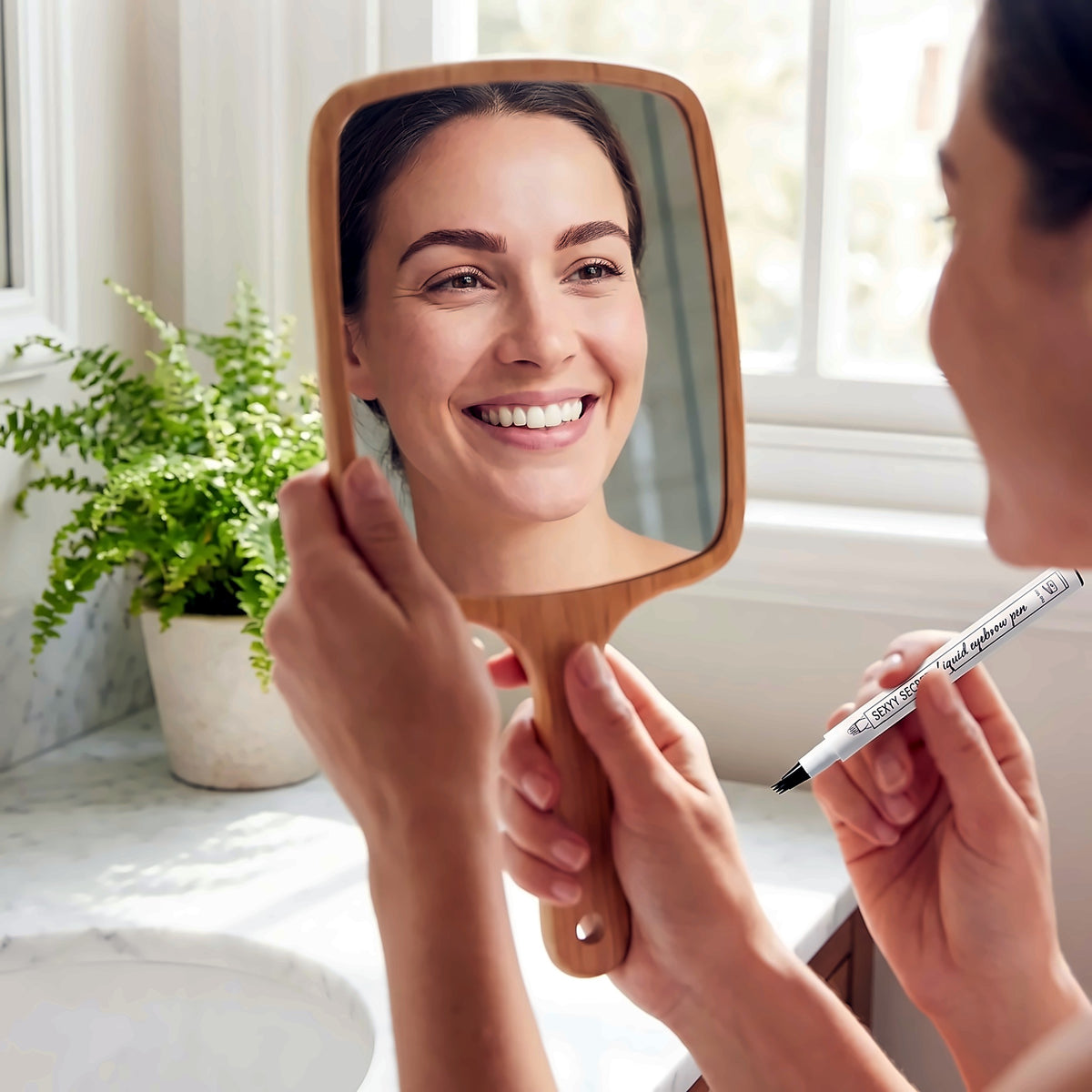 Woman checking her brows in a hand mirror